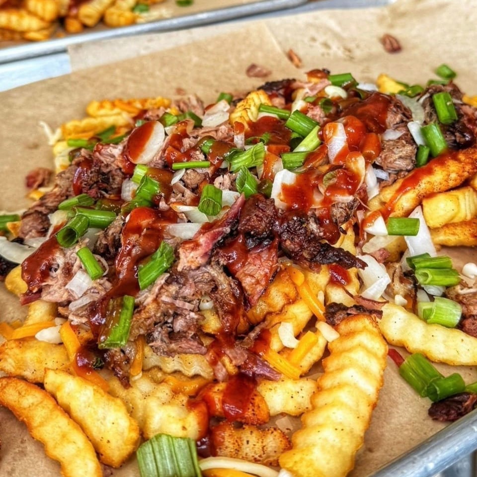 Close-up of loaded crinkle-cut fries with pulled pork, cheese, onions, scallions, and barbecue sauce.