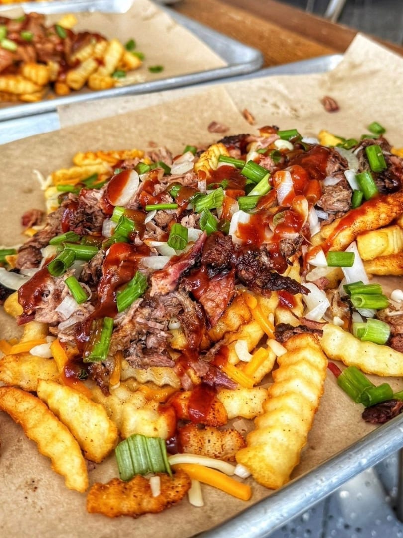 Close-up of loaded crinkle-cut fries with pulled pork, cheese, onions, scallions, and barbecue sauce.