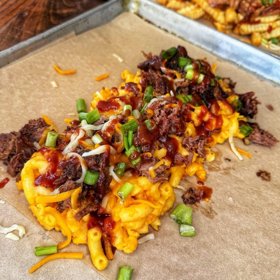Macaroni and cheese topped with pulled pork, BBQ sauce, shredded cheese, and green onions on a tray.