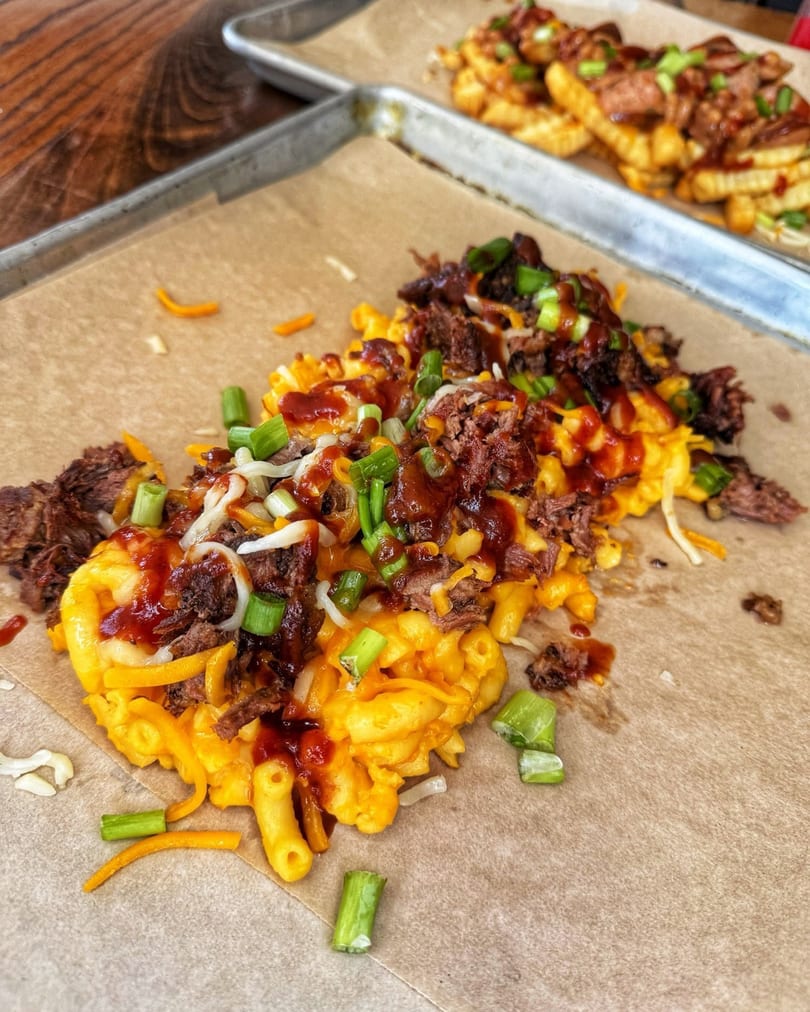 Macaroni and cheese topped with pulled pork, BBQ sauce, shredded cheese, and green onions on a tray.