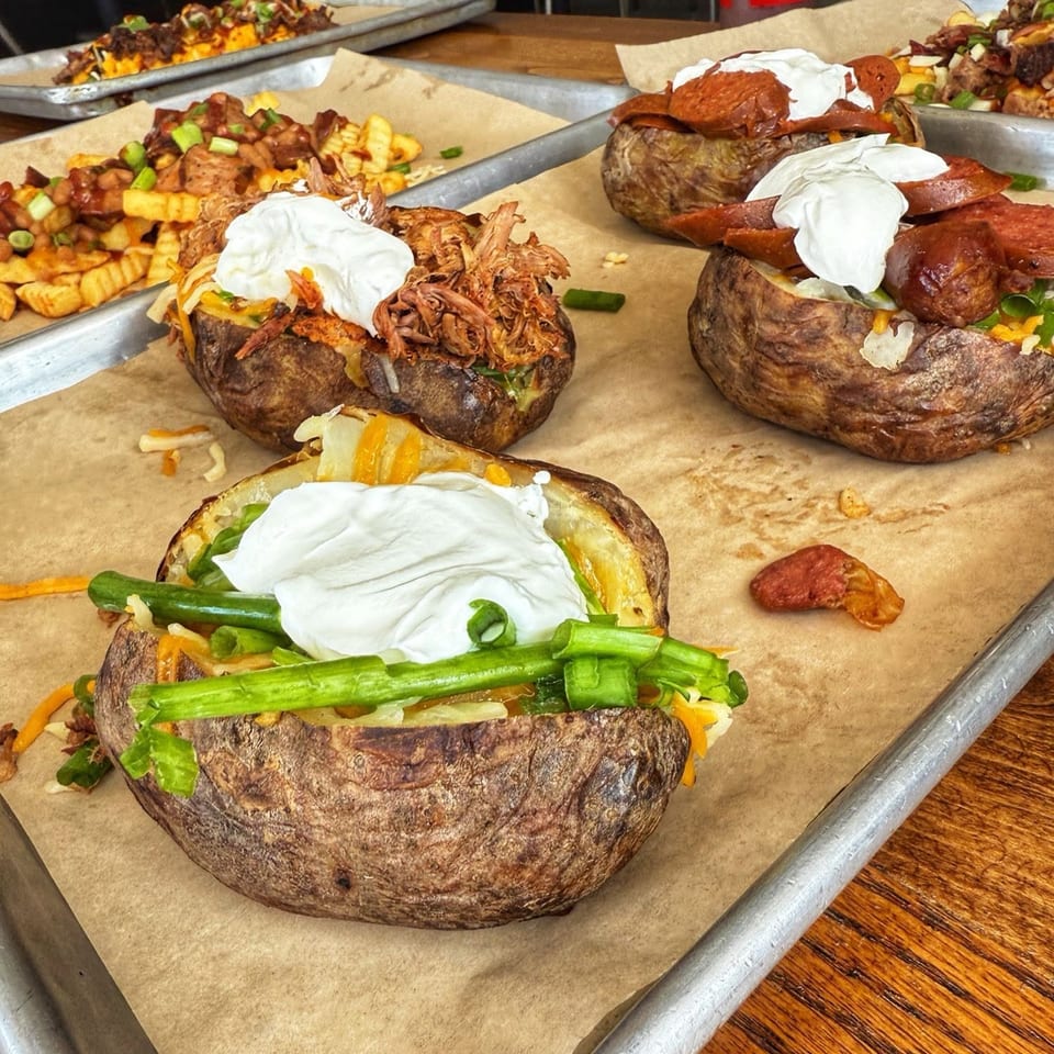Baked potatoes with various toppings like pulled pork, pepperoni, and green onions on a tray.