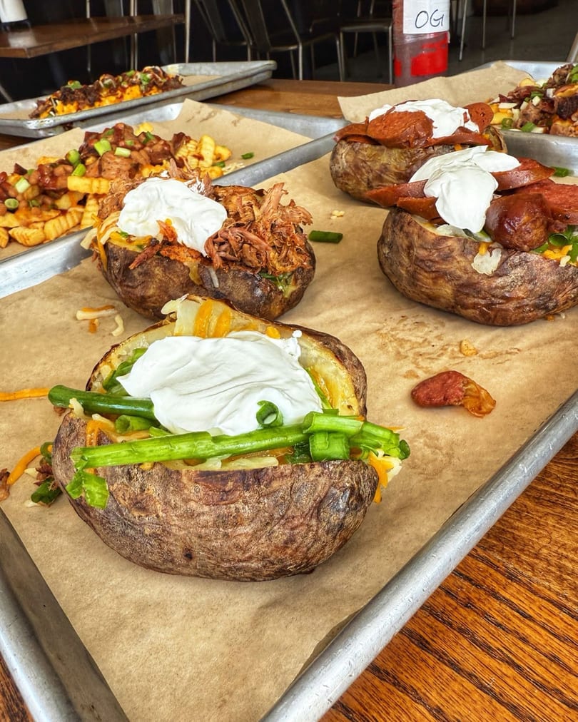 Baked potatoes with various toppings like pulled pork, pepperoni, and green onions on a tray.